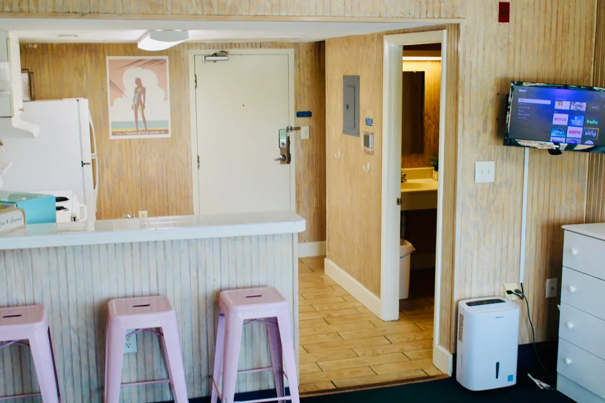 A friendly, open kitchen area with a central island and stools, retro-style poster art, and a glimpse into the adjacent bathroom. The space is designed for gathering, sharing meals, and easy transitions between activities—central to an efficient studio layout.